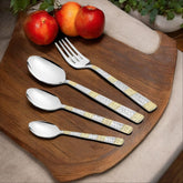 Elegant cutlery with gold and silver handles displayed on wooden tray beside fresh red fruits.